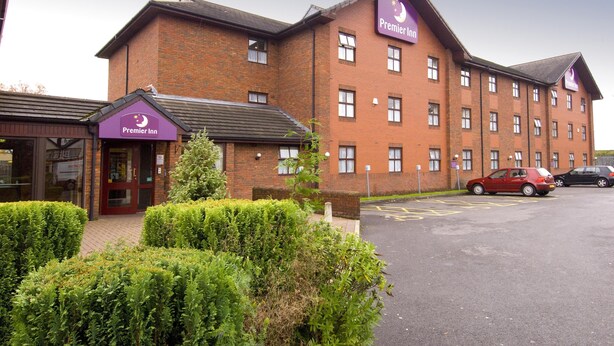 Un hotel Premier Inn con facciata in mattoni, numerose finestre e un'area di parcheggio con auto.