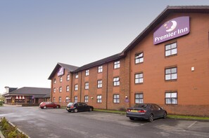 A brick building with a 'Premier Inn' sign, multiple windows, and parked cars. - Premier Inn Manchester - Prestwich (Manchester)