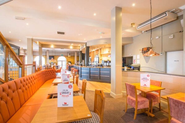 Un restaurante con una barra larga, zona de estar con bancos acolchados y un área de bar.