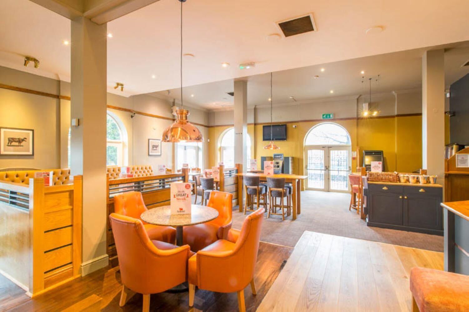 A restaurant with round tables, orange chairs, a bar area, and a television screen.
