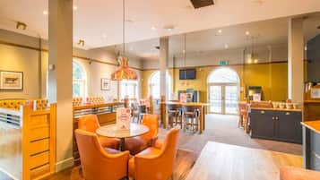 A restaurant with round tables, orange chairs, a bar area, and a television screen.