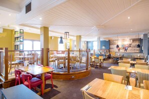 A restaurant with multiple dining areas, including a central round table surrounded by chairs and a separate dining section with individual tables and chairs. - Premier Inn Manchester Salford Quays (Salford)