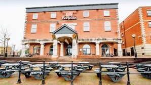 A red brick building with a sign reading 'Beefeater' and 'GUAY HOUSE' on the ground floor. There are outdoor tables and benches in front.