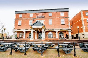 A red brick building with a sign reading 'Beefeater' and 'GUAY HOUSE' on the ground floor. There are outdoor tables and benches in front.