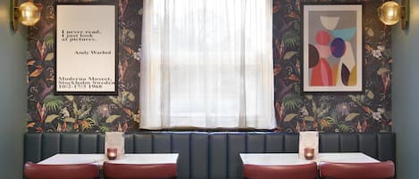 A restaurant interior with a booth seating area, tables, and wall art.