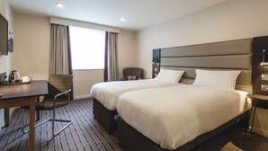 Camera d'albergo con due letti, una scrivania con un bollitore, una sedia e una finestra con tende.