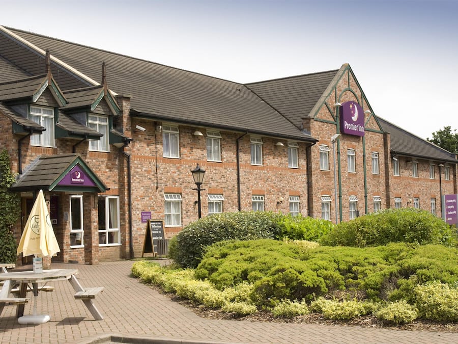 En byggnad i tegel med en skylt för Premier Inn, utomhusservering och en välskött trädgård.