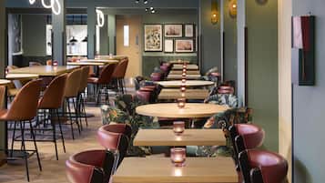 L’intérieur d’un restaurant avec des tables rondes, des chaises rembourrées et des lampes suspendues fixées au mur.