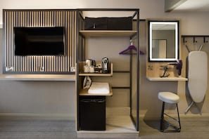Una habitación de hotel compacta con televisión de pantalla plana, una kitchenette pequeña, un espejo y una tabla de planchar plegable.
