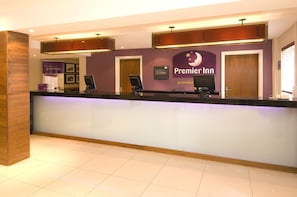 A hotel reception desk with a 'Premier Inn' sign, a computer, and a counter. - Premier Inn Manchester Old Trafford (Manchester)