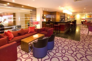 A hotel lobby with a red sofa set, a wooden coffee table, and a patterned carpet.