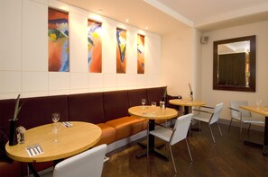 L’intérieur d’un restaurant avec un long banc brun, des tables rondes et des chaises blanches.