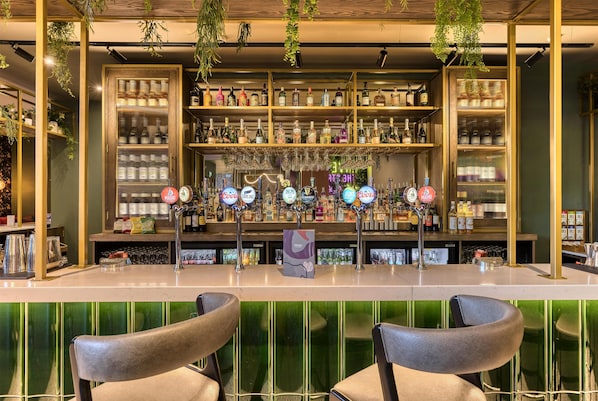 A bar area with a counter, bar stools, and shelves stocked with bottles and glasses. - Premier Inn Manchester City - Piccadilly (Manchester)