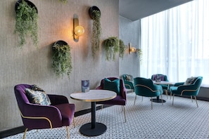 A modern interior with hanging plants, purple and teal chairs, a round table, and patterned flooring. - Premier Inn Manchester City - Piccadilly (Manchester)