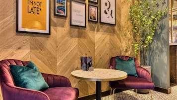 A room with two purple armchairs, a round table, and framed artwork on the wall.