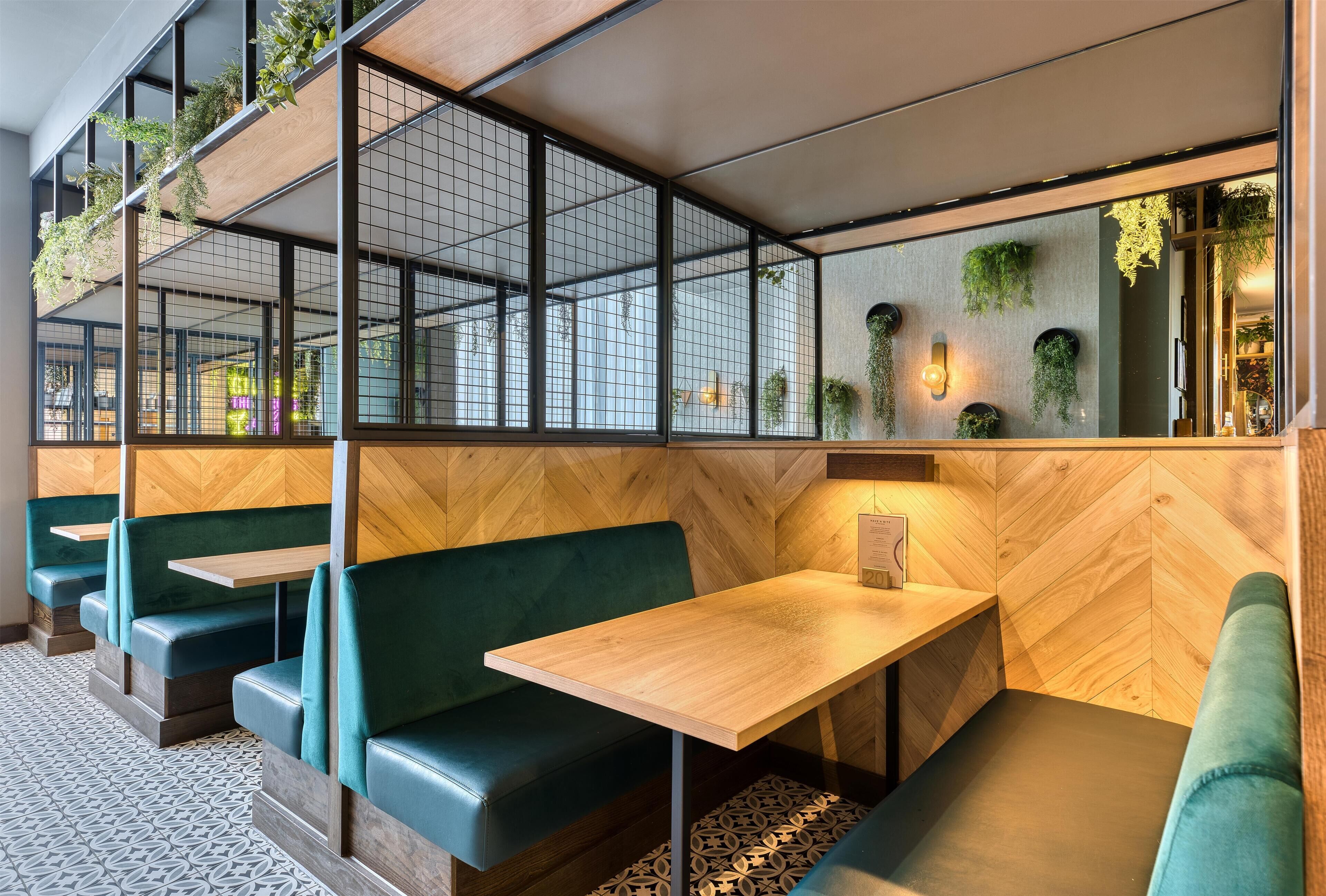 A restaurant interior with green booths, wooden tables, and hanging plants.