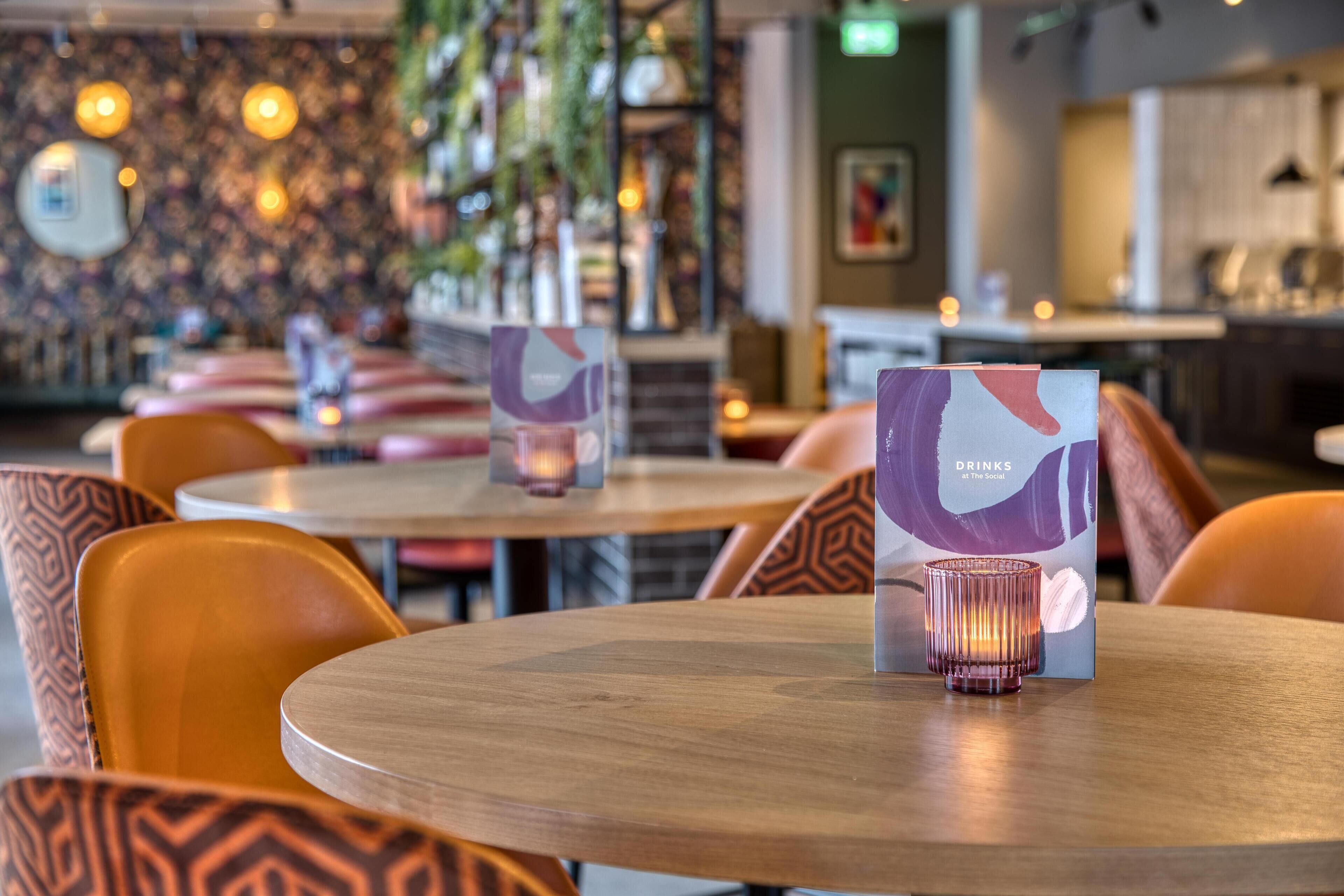 Un interior de restaurante con mesas redondas, sillas estampadas color naranja y un atril con una vela.