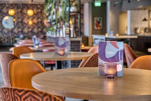 L’intérieur d’un restaurant avec des tables rondes, des chaises à motifs orange et un présentoir à menus agrémenté d’une bougie.