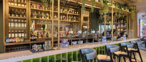 Un espace bar avec des étagères remplies de bouteilles, de verres et d’ustensiles de bar. On y trouve des tabourets de bar et un comptoir.