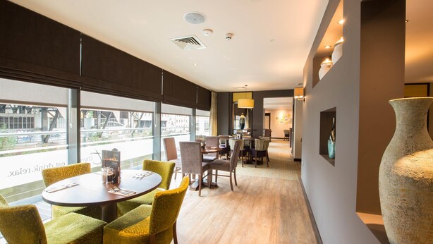 Una habitación de hotel moderna con comedor, ventanas amplias y un jarrón grande.