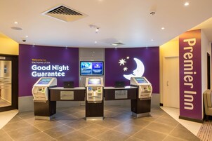 A hotel reception area with a purple wall, a monitor displaying information, and three check-in kiosks.