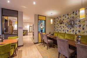 A hotel lobby with a dining area, a reception desk, and a wall with a sunburst mirror. - Premier Inn Manchester City Centre West (Salford)