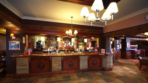 Uma área de bar com chão quadriculado, balcão de madeira e várias luminárias.