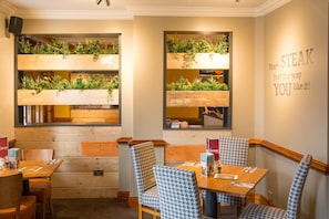 A restaurant interior with wooden panel walls, houndstooth patterned chairs, and green plants on shelves. - Premier Inn Durham East (Durham)