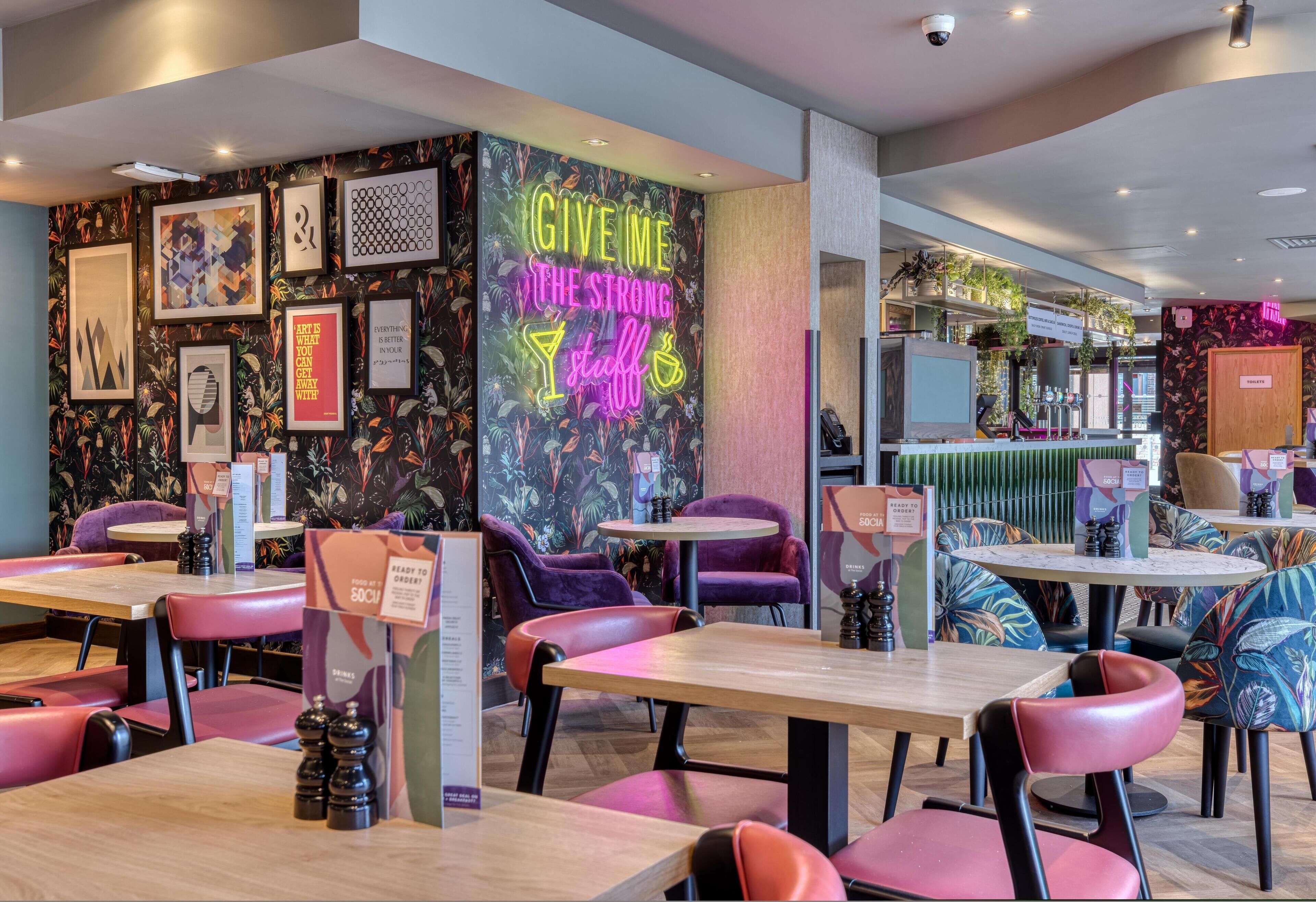 A restaurant interior with tables, chairs, and a neon sign on the wall.