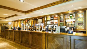 Een bar met houten lambrisering, een klok en verschillende flessen en glazen.