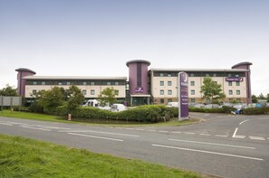 A hotel with a prominent 'Premier Inn' sign, a parking area, and a clear sky.