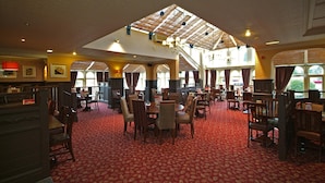 Un hall d’hôtel spacieux, doté de hauts plafonds, de grandes fenêtres et d’un tapis rouge à motifs.