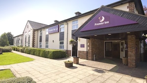 L’entrée d’un hôtel, avec une enseigne indiquant « Premier Inn », un chemin piétonnier aménagé et un petit espace jardin.