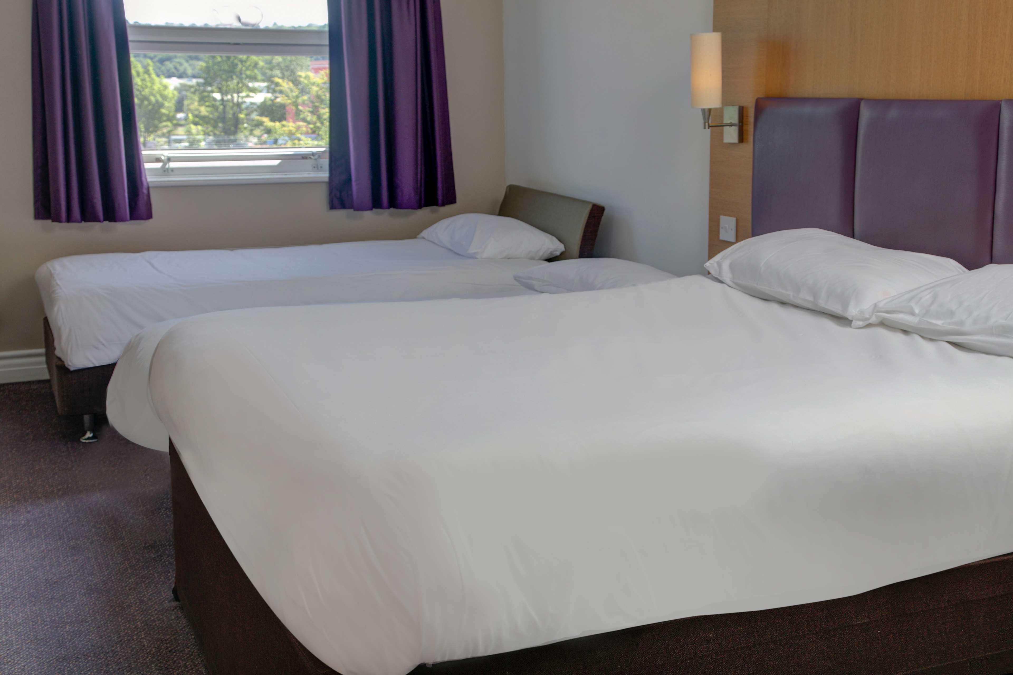 Una habitación de hotel con dos camas individuales, una ventana con cortinas moradas y una lámpara fijada a la pared.