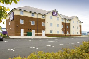 Un hotel de varios pisos con un llamativo letrero de Premier Inn, un estacionamiento con flechas direccionales y un cielo despejado.