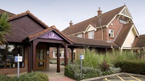 Um edifício com a placa 'Premier Inn', uma área de estacionamento e uma placa de rua 'Roman Way'.