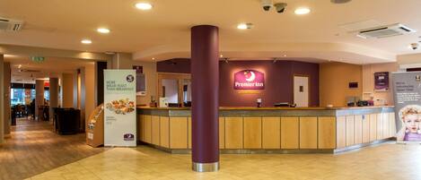 A hotel reception area with a prominent Premier Inn sign, a reception desk, and a pillar.
