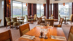A dining area with multiple tables and chairs, large windows, and a view of the outdoors. - Premier Inn Nottingham Arena - London Road (Nottingham)