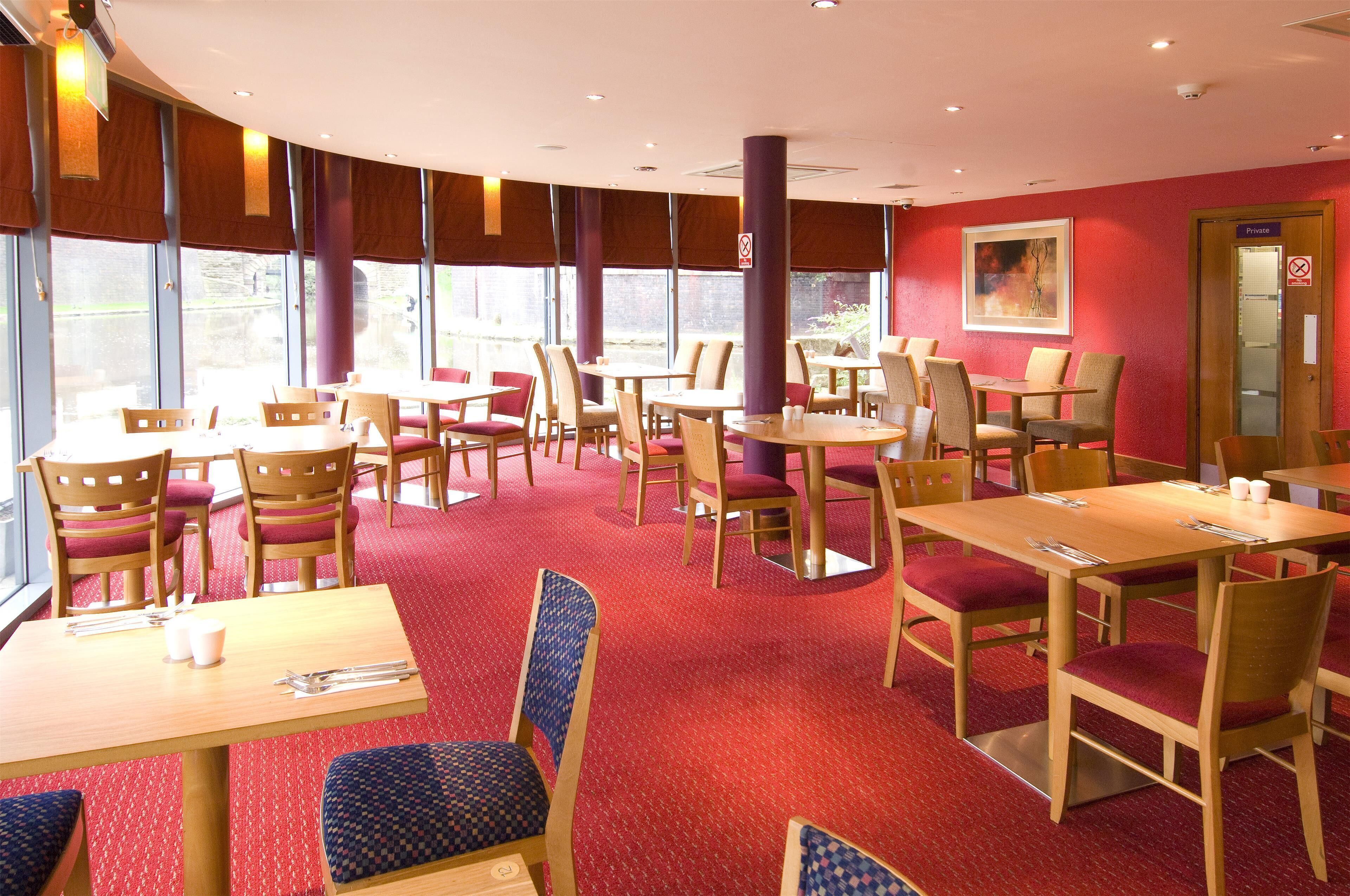 Een restaurant met ronde tafels en stoelen, een vloer met rood tapijt en grote ramen.