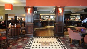 A bar area with wooden furniture, a patterned floor, and a bar counter. - Premier Inn Leicester North West (Leicester)