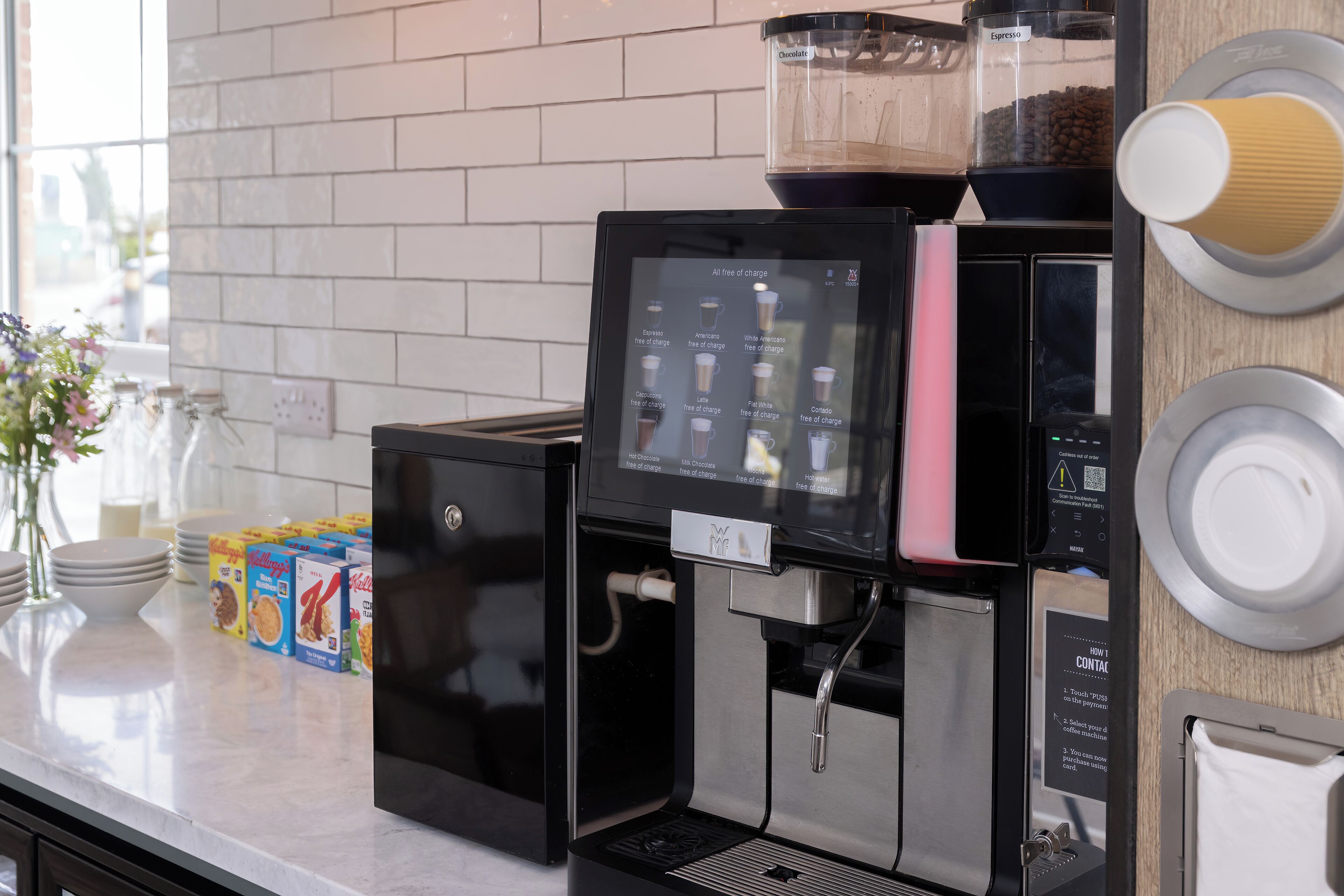 Una cafetera con pantalla digital, un molinillo de café y un espumador de leche sobre una encimera de cocina.