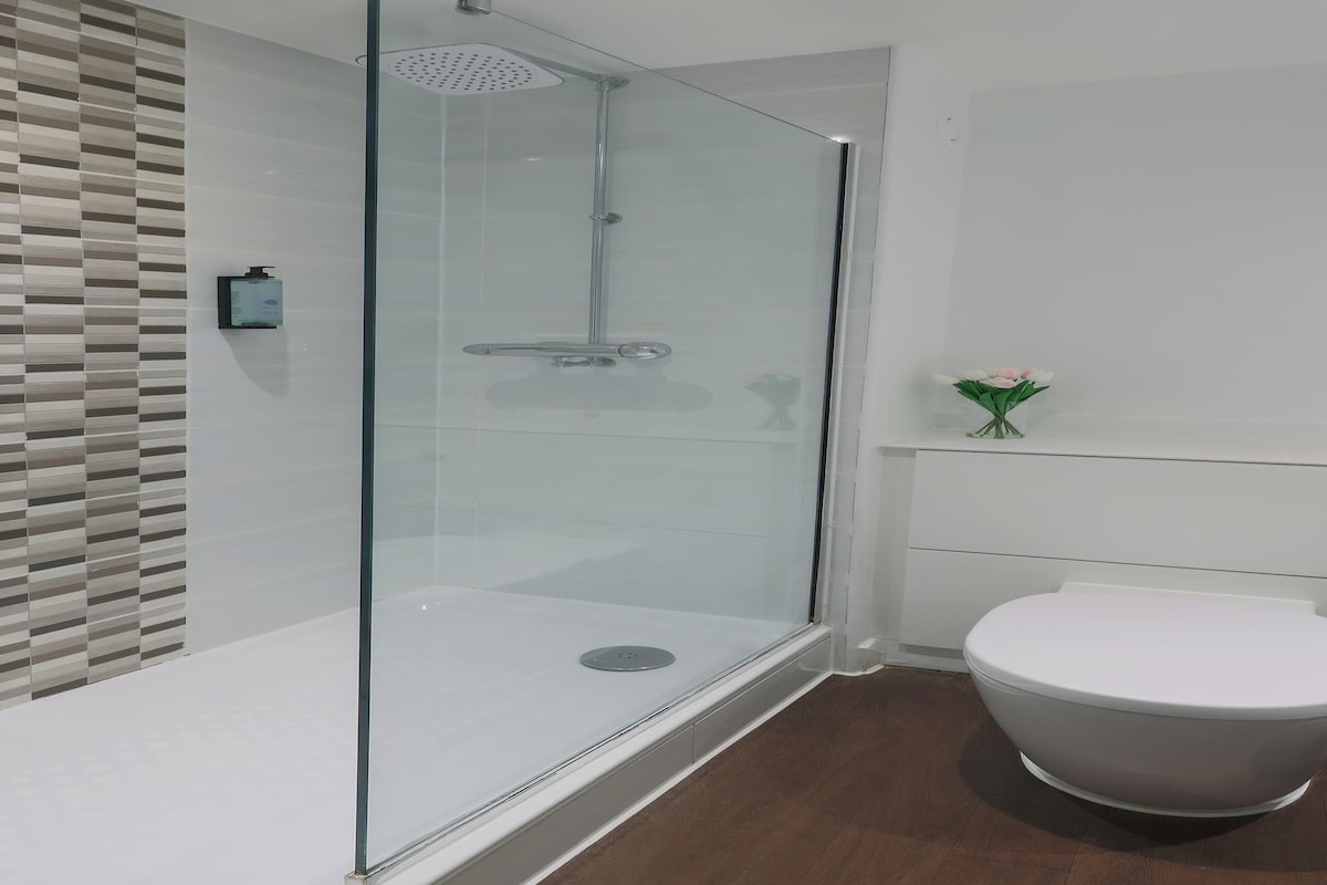 A modern bathroom with a glass-enclosed shower, a toilet, and a small vase of flowers on the vanity.