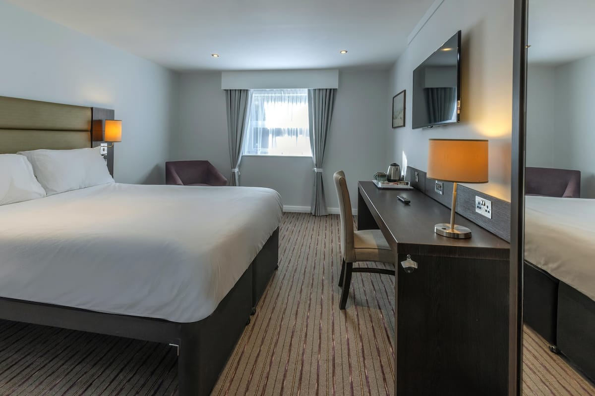 Een hotelkamer met een groot bed, een bureau, een stoel, een televisie en een raam met gordijnen.