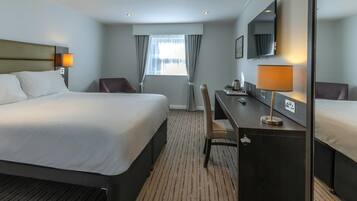 A hotel room with a large bed, a desk, a chair, a TV, and a window with curtains.