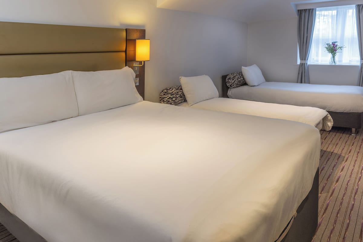 Hotelkamer met twee bedden, een hoofdbord, een bedlampje, een raam met gordijnen en een vloerbedekking.
