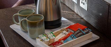 A tray with tea bags, a kettle, and two mugs on a marble table.