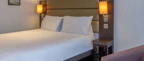 Una habitación de hotel con una cama, dos lámparas de noche, una mesita de noche y una silla.