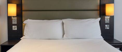 A neatly made bed with white linens, a dark headboard, and two wall-mounted lamps on either side.