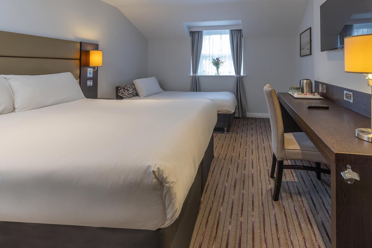 Een hotelkamer met een groot bed, een bureau met stoel, een raam met gordijnen en een wandtelevisie.