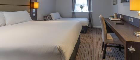 Habitación de hotel con una cama grande, un escritorio con silla, una ventana con cortinas y un televisor montado.